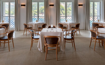 Dining room at Aman Sveti Stefan with wooden chairs and tables beside tall windows.