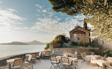 Dining piazza at Aman Sveti Stefan overlooking the Adriatic Sea with white chairs and flowering trees.