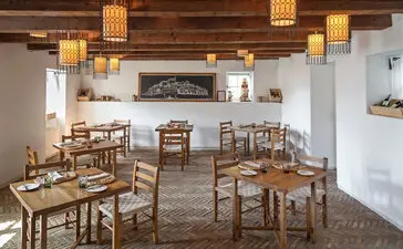Dining piazza at Aman Sveti Stefan with wooden tables and chairs beneath pendant lighting.