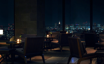 Aman Tokyo's dining lounge at dusk, with warm lighting and Tokyo's cityscape glowing beyond floor-to-ceiling windows.