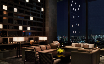 Aman Tokyo dining lounge at dusk with floor-to-ceiling windows overlooking the city skyline, warm lighting and contemporary seating.