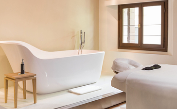 アマン ヴェニスのバスルーム。白い浴槽、木製の梁、テラコッタタイルの床。