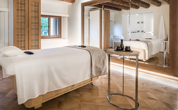 Chambre spacieuse à Aman Venice avec lit king-size aux draps blancs et miroir mural reflétant la lumière naturelle.