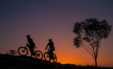 Silhouettes of two cyclists with bikes against an orange sunset sky at Amandari.