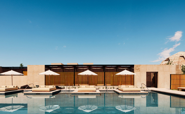 Amangiri's pool at sunset with desert pavilions and clear blue sky.