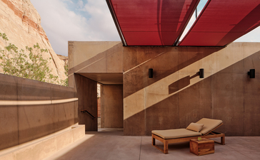 Amangiri camp shelter with red canopy and wooden seating in desert landscape.