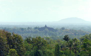 Misty morning landscape at Amanjiwo, with forested hills and distant volcanic peaks.