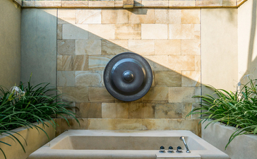 Outdoor bathtub with circular water feature at Amanjiwo resort, framed by stone walls and green foliage.