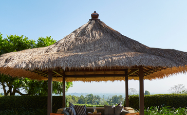 Pavillon au toit de chaume avec mobilier en bois au resort Amanjiwo, vue sur la vallée