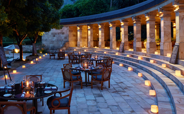 Terrasse illuminée du resort Amanjiwo avec colonnes voûtées, piscine et mobilier élégant au crépuscule.