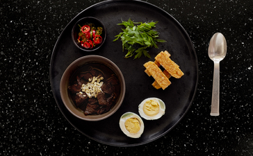 Amanjiwo dining experience: soup bowl with garnish, fresh herbs, citrus slices, and breadsticks arranged on dark plate.