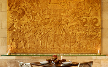 Circular dining table with two chairs beneath a large golden abstract artwork at Amanjiwo.