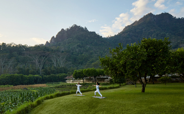 Two guests seated on the lawn at Amanjiwo, with verdant rice terraces and forested mountains beyond.