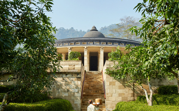 A stone pavilion with a domed roof framed by trees at Amanjiwo, with a figure walking along the central pathway.