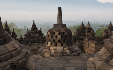 Stone stupas at Amanjiwo with misty volcanic peaks beyond, Java, Indonesia.