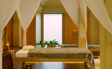 Amanjiwo spa treatment room with draped fabric ceiling, wooden pillars, and massage bed adorned with fresh flowers.