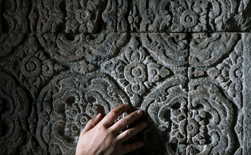 Hand touching ornate carved stone detail at Amanjiwo.