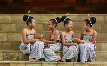 Four Balinese dancers in traditional dress sit together on stone steps at Amanjiwo resort.