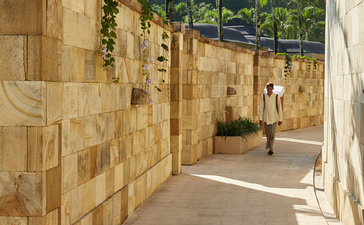 Corridor pavée bordée de murs en pierre avec végétation tropicale, Amanjiwo resort.