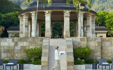 Amanjiwo's domed pavilion reflected in a still pool, framed by columns and tropical palms against verdant hillsides.