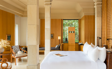 Principal bedroom at Amanjiwo with white bed, stone columns and wooden door.