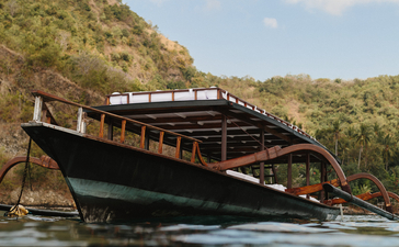 Traditional wooden boat moored in calm waters at Amankila, surrounded by lush hillside vegetation.