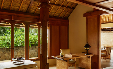 Balinese-style principal bedroom with wooden beams and pillars at Amankila resort, featuring large windows overlooking tropical gardens.