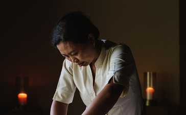 Balinese massage therapy session at Amankila resort, therapist working on guest's leg by candlelight.
