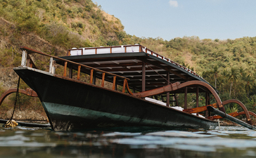 Wooden longtail boat moored in turquoise waters at Amankila resort, with forested hillside beyond.