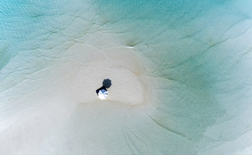 Aerial view of a traditional outrigger boat on turquoise shallow waters at Amanpulo.