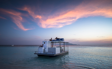 Catamaran anchored in calm waters at Amanpulo at sunset, with pink and purple clouds reflected on the sea.