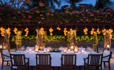 Candlelit dining table set beneath string lights at Amanpulo at dusk.