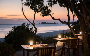 Dining pavilion at Amanpulo at dusk, with candlelit table overlooking calm waters at sunset.