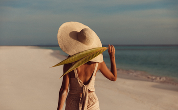 アマンプロ リゾートのビーチで麦わら帽子をかぶり、肩越しに海を眺める人。