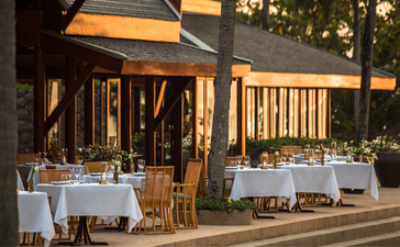 Amanpuri resort dining venue with elegantly set tables beneath a covered pavilion at dusk.