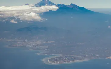 Aerial view of Amanwana's island setting, with volcanic mountain rising above clouds and surrounding turquoise waters.