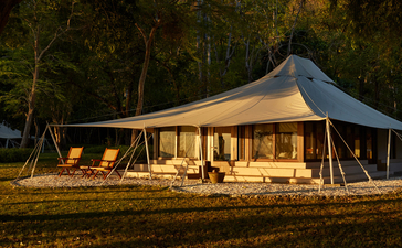 安缦湾澜度假村的帐篷式住宿在夜幕中温暖发光，周围被树木环绕。