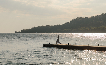 Wooden jetty extending into calm sea at Amanwana, with forested shoreline beyond.