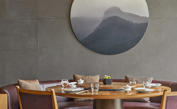 Dining table and wooden chairs beneath a circular window framing mountain views at Amanyangyun.