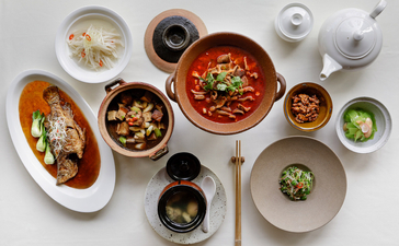 Overhead view of various Asian dishes at Amanyangyun, including noodles, stir-fries, and soups in white and grey bowls.
