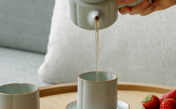 Hand pouring tea at Amanyangyun, with ceramic cups and bowls of nuts and berries on table.