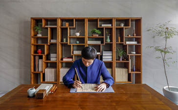 Woman in blue shirt seated at wooden desk in front of built-in shelving at Amanyangyun.