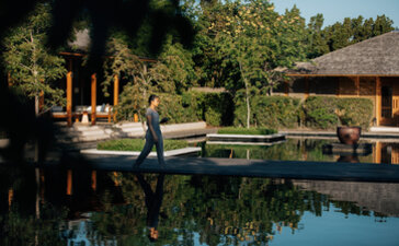 Infinity pool reflecting surrounding trees at Amanyara, with thatched-roof pavilions beyond.