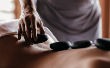 Therapist's hands placing heated stones on a guest's back during a wellness treatment at Amanyara.