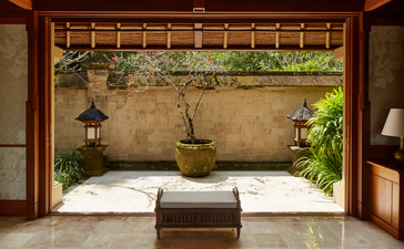 Amandari resort two-bedroom suite with open courtyard featuring a bed, stone walls and potted plants.