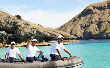 Crew in dinghy at Amandira, Indonesia, with turquoise waters and rocky islands.