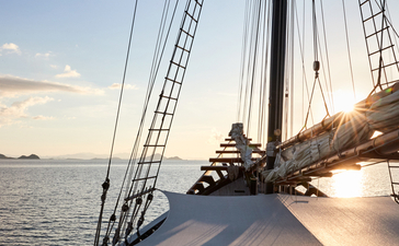 Wooden deck of a sailing vessel at Amandira, Indonesia, with rigging and sails visible at sundown over calm waters.