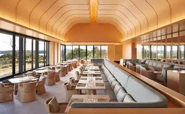 Amanemu's dining venue with wooden barrel-vaulted ceiling, floor-to-ceiling windows overlooking gardens, and tables set for service.