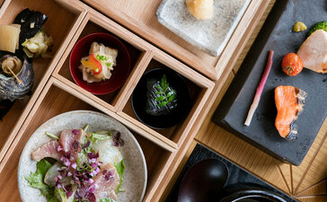Vista aérea del comedor de Amanemu, mostrando platos con carne, verduras y flores comestibles en vajilla minimalista.