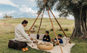 アマンジェナ リゾートで、家族が大きな木の下にテントを張り、一緒に時間を過ごしている。